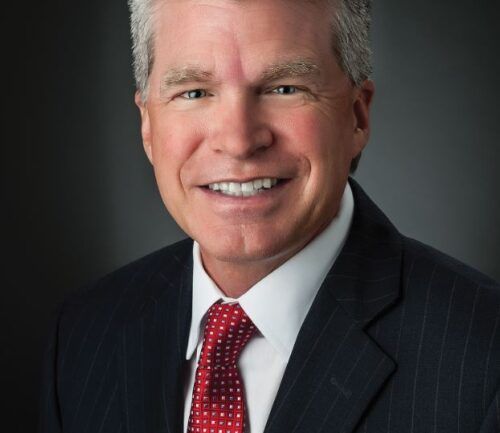 Professional headshot of Wally Sackett in dark suit with red patterned tie