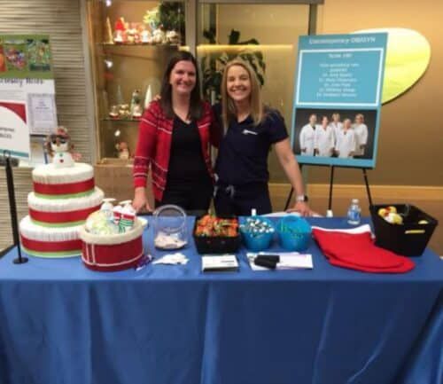 Two healthcare staff members standing behind informational table with cake and promotional materials