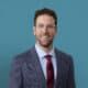 Professional headshot of Dr. Zachary Miller in gray suit with burgundy tie