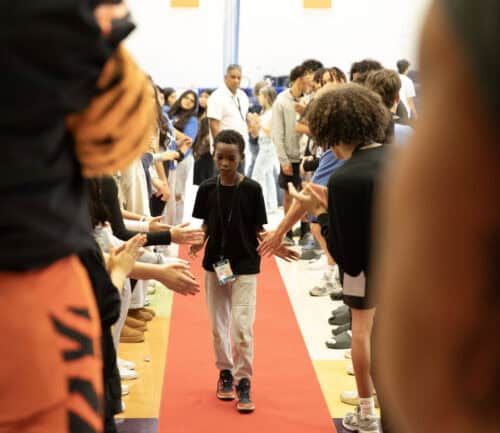 Young person walking down red carpet while crowd applauds with outstretched hands