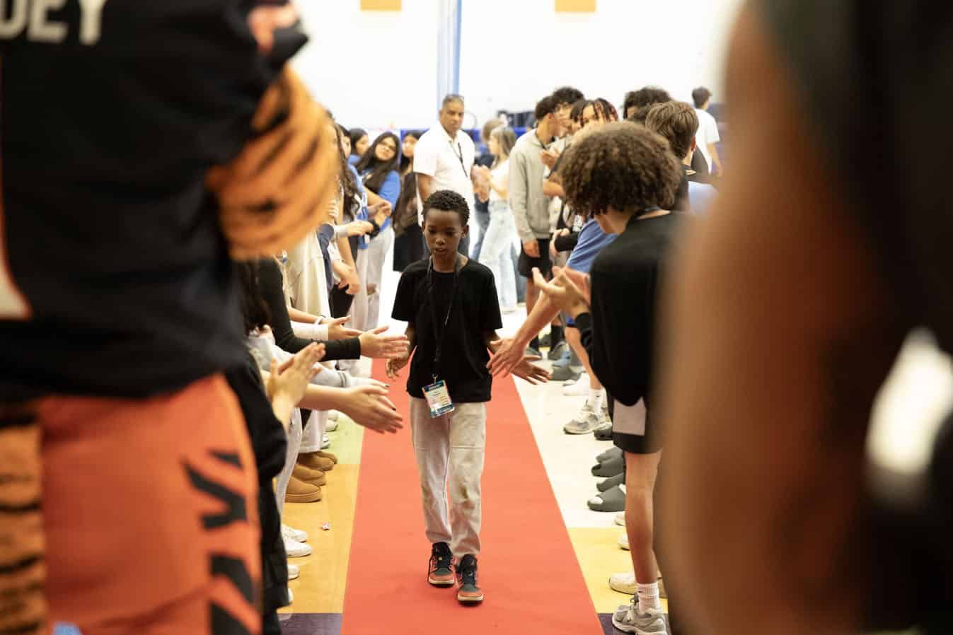 Young person walking down red carpet while crowd applauds with outstretched hands