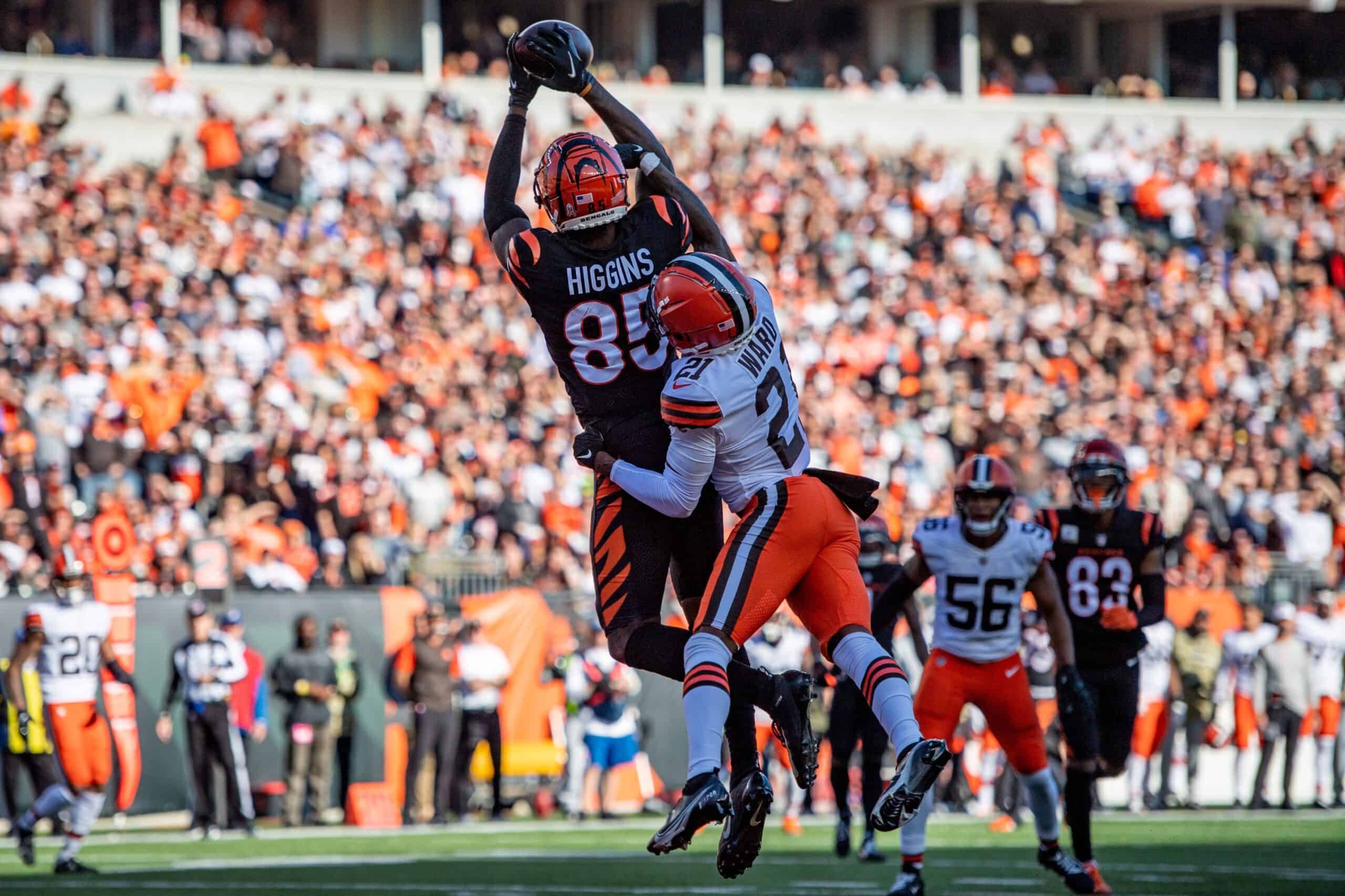 Football player in black uniform catches ball while defender in orange attempts tackle