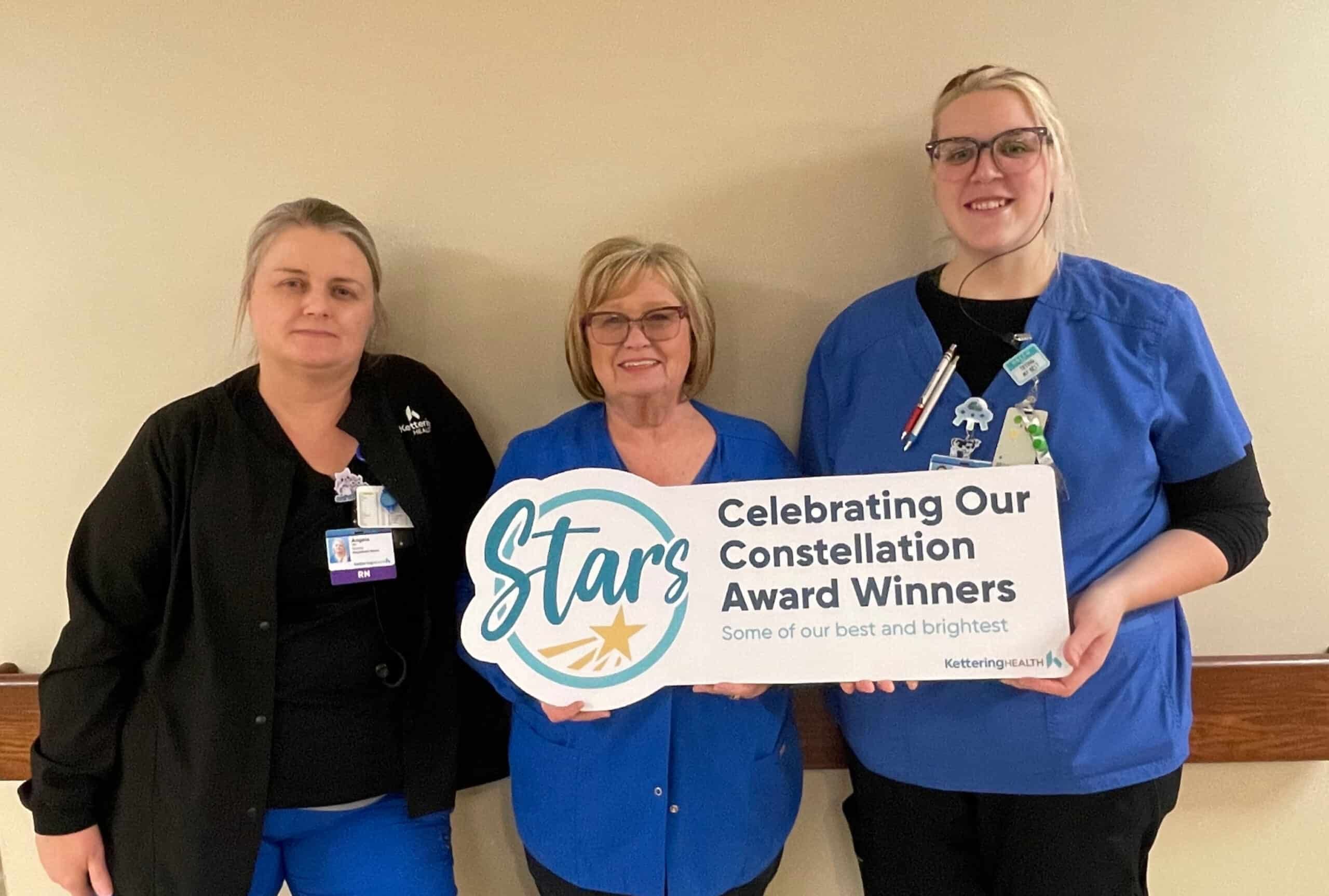 Three healthcare workers holding Constellation Award Winners banner celebrating staff recognition