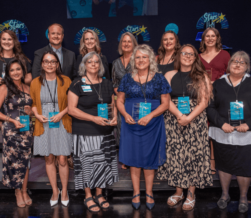Healthcare award recipients holding blue plaques at recognition ceremony on stage