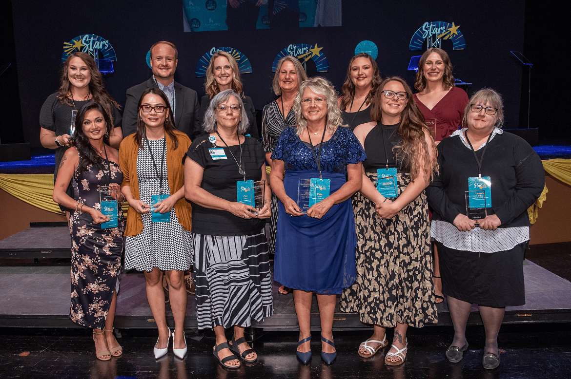 Healthcare award recipients holding blue plaques at recognition ceremony on stage