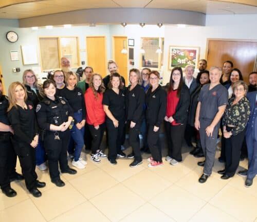 Large group of healthcare workers and emergency responders posing together in hospital lobby