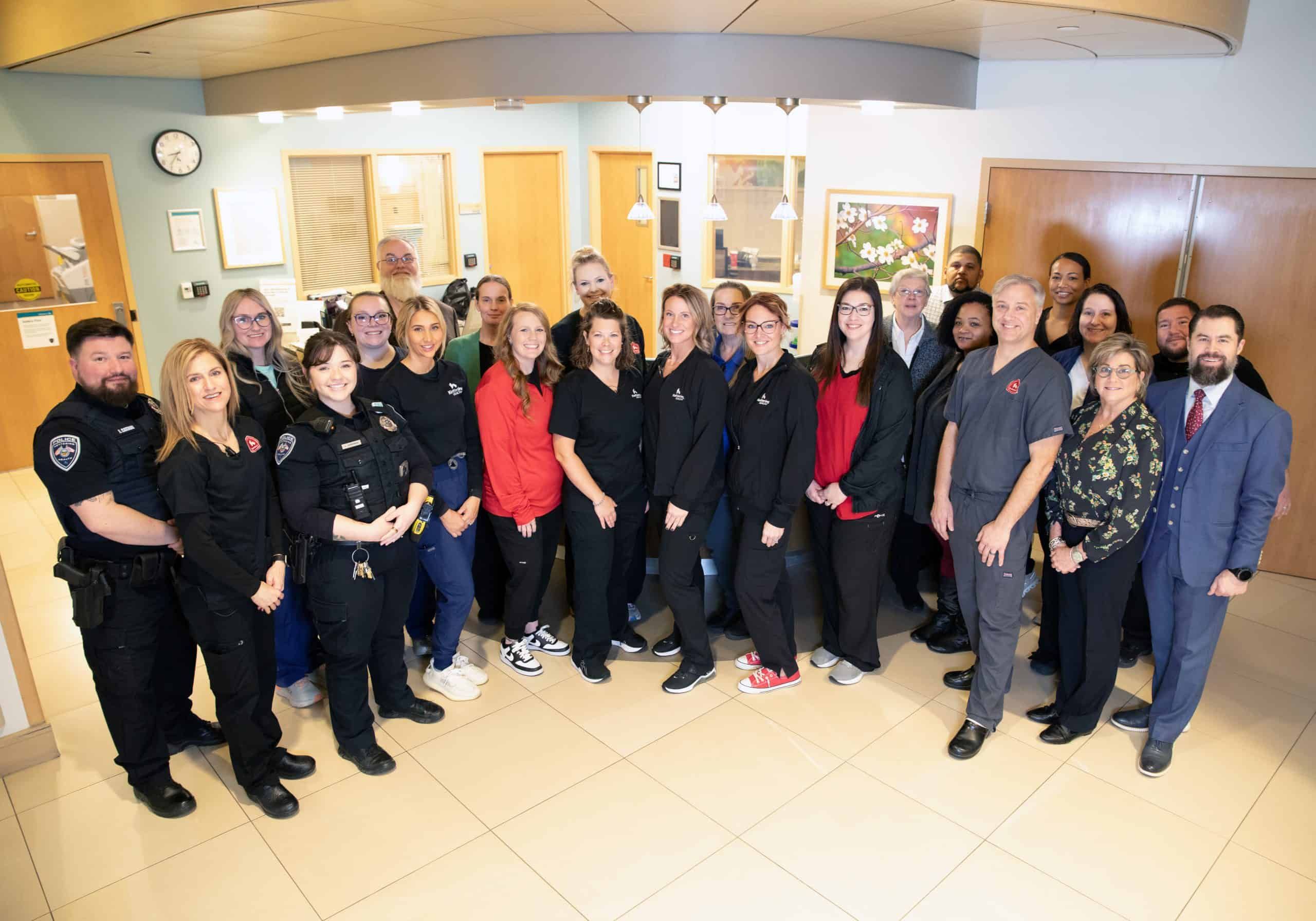 Large group of healthcare workers and emergency responders posing together in hospital lobby