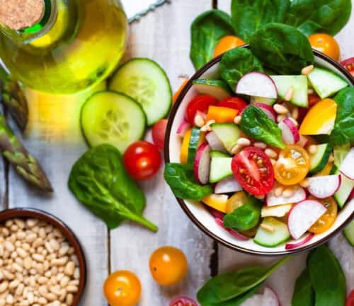 Fresh vegetable salad bowl with spinach, tomatoes, cucumbers, and olive oil on wooden surface