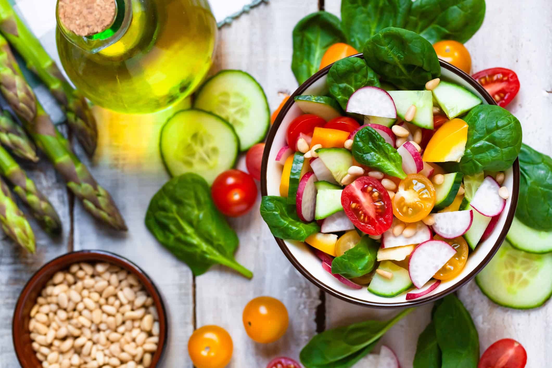 Fresh vegetable salad bowl with spinach, tomatoes, cucumbers, and olive oil on wooden surface