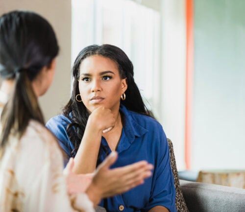Female therapist listening attentively as patient gestures during healthcare consultation session.