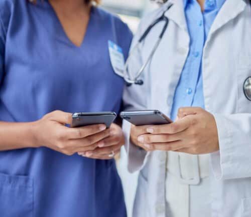Two healthcare professionals in scrubs and white coat using smartphones together