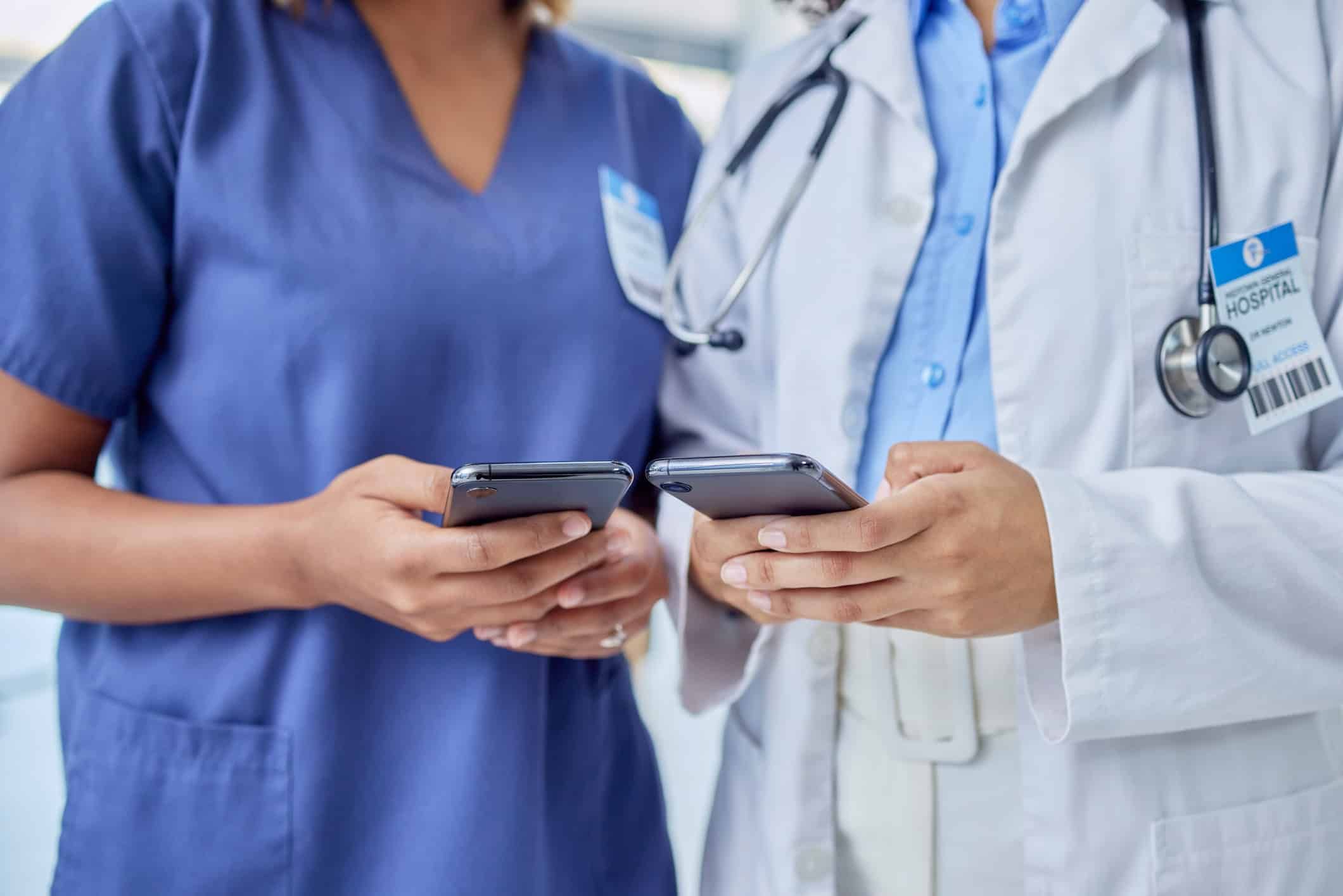 Two healthcare professionals in scrubs and white coat using smartphones together