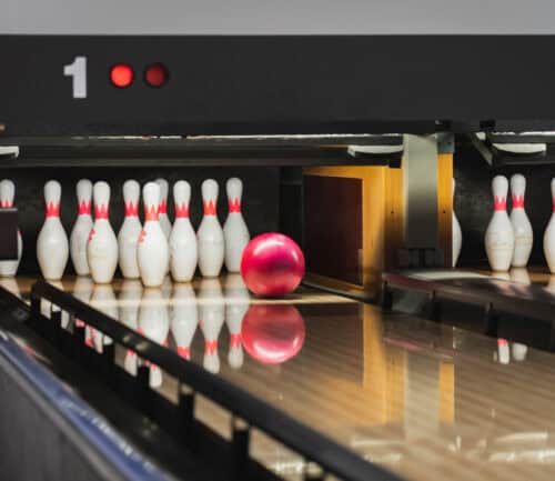 Red bowling ball rolling toward white pins on polished lane at bowling alley.