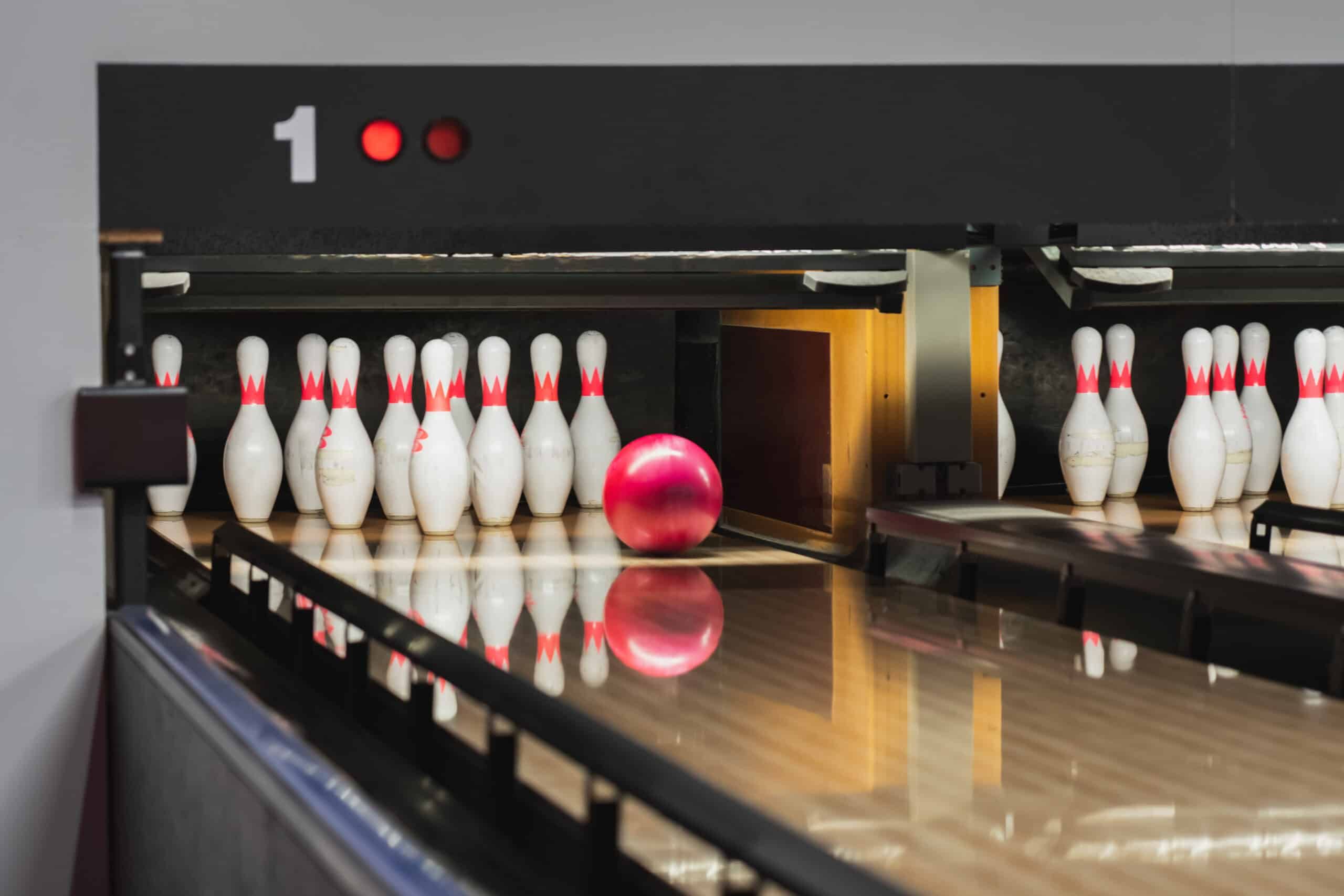 Red bowling ball rolling toward white pins on polished lane at bowling alley.