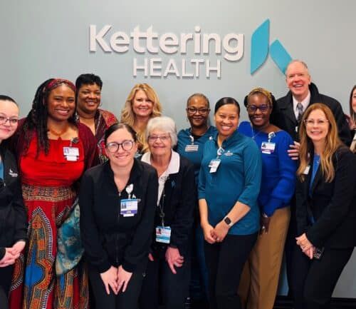Group of Kettering Health employees posing together in front of company logo wall