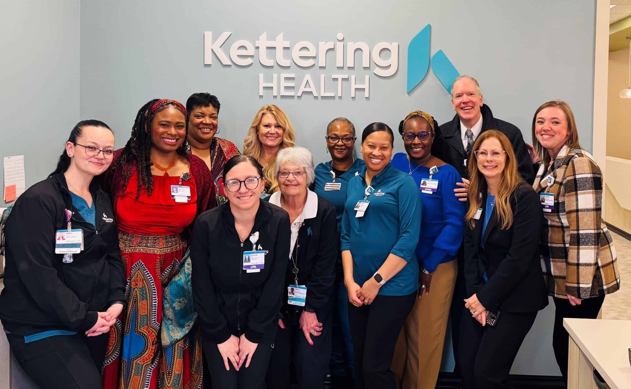 Group of Kettering Health employees posing together in front of company logo wall
