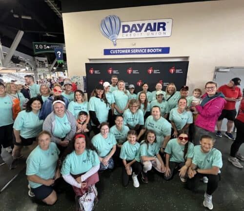 Large group of volunteers in matching light green shirts posing at DayAir Credit Union booth
