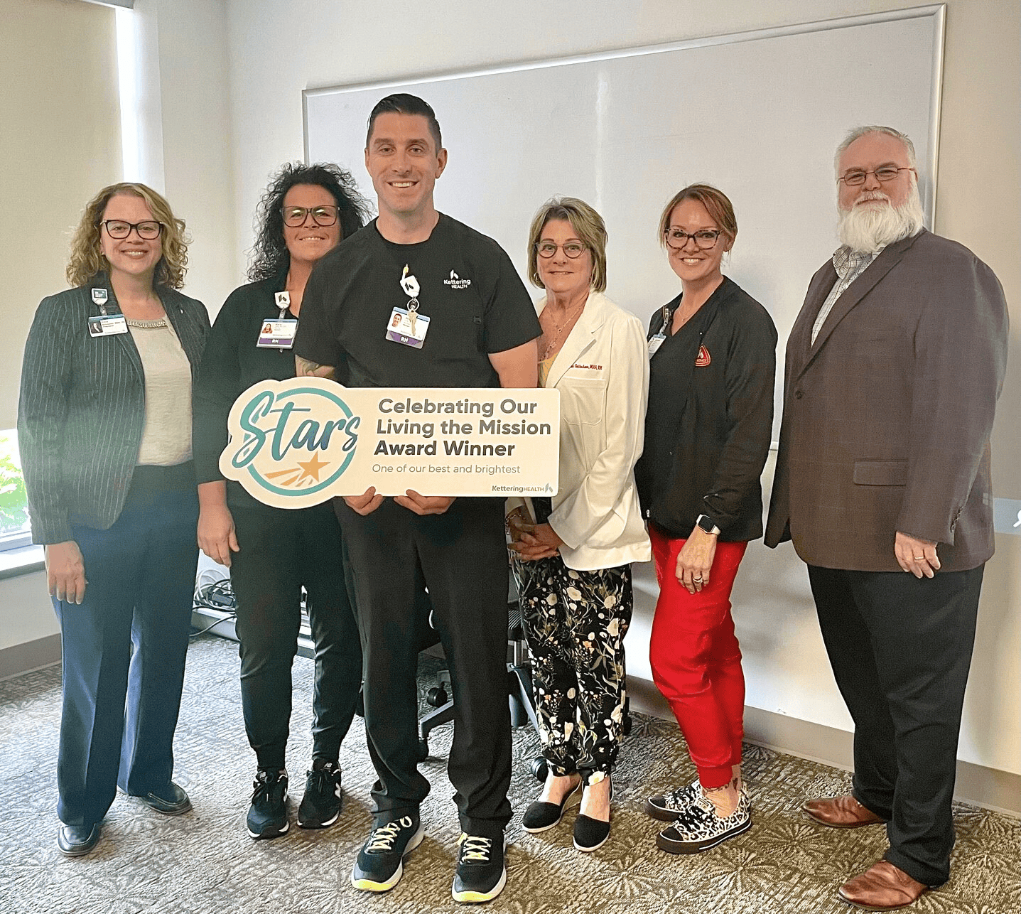 Six healthcare professionals celebrating Joey Brumfield's "Living the Mission" Star Award with ceremonial sign