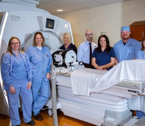 Medical team posing with SIGNA Architect MRI machine and hospital bed equipment