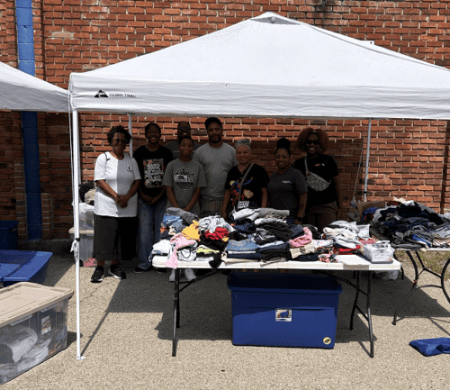 Group of volunteers organizing donated clothing under white tent at community event