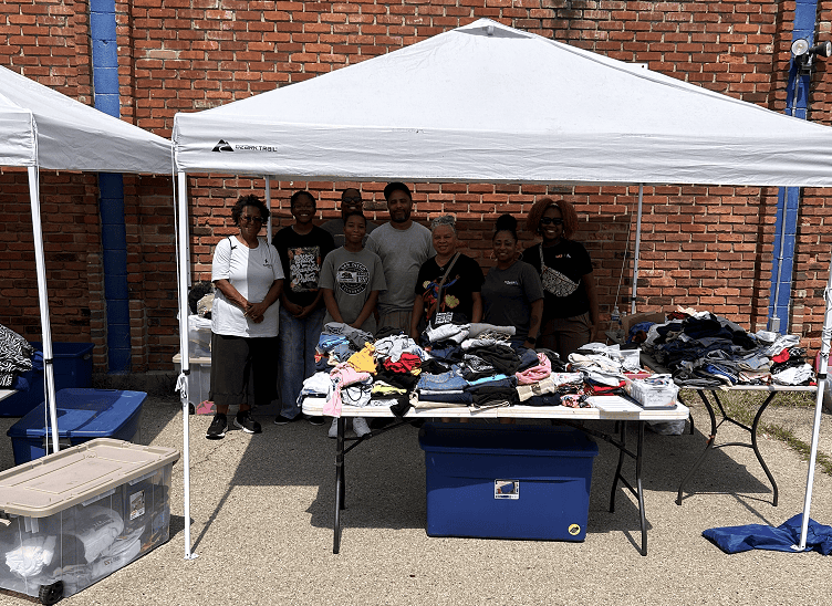 Group of volunteers organizing donated clothing under white tent at community event
