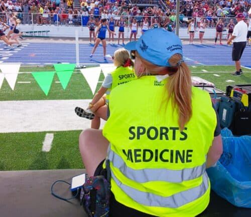 Sports medicine professional in bright yellow vest attending to athlete at track and field event