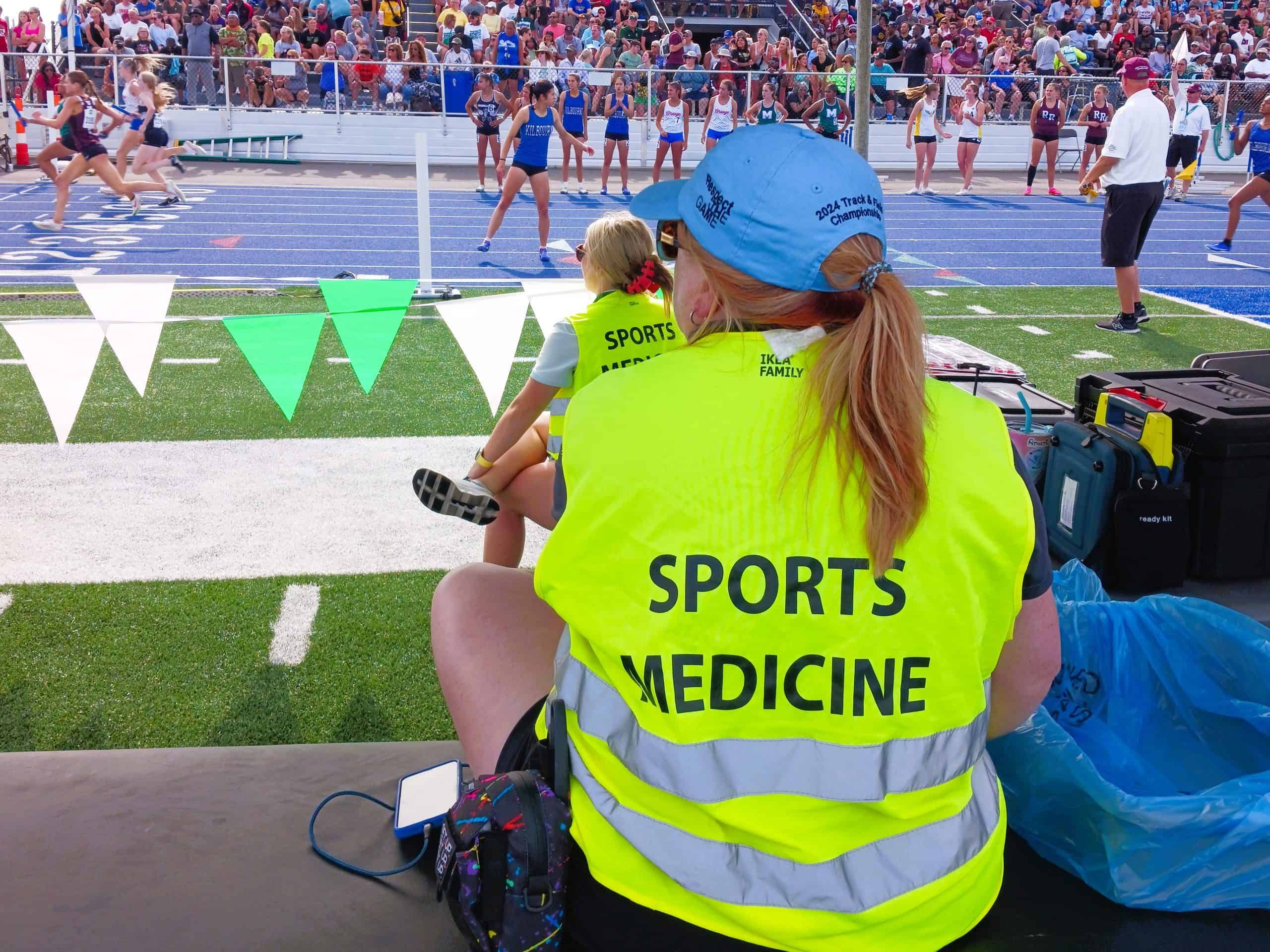 Sports medicine professional in bright yellow vest attending to athlete at track and field event