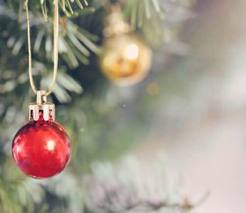 Red Christmas ornament hanging on evergreen tree branch with blurred holiday lights