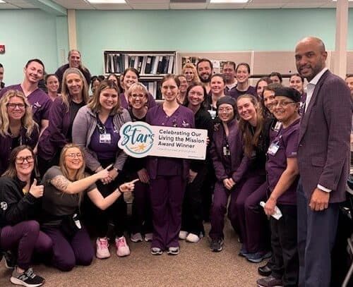 Healthcare team celebrates award with "Living the Mission Award Winner" banner