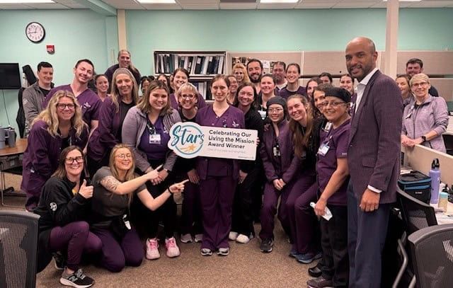 Healthcare team celebrates award with "Living the Mission Award Winner" banner