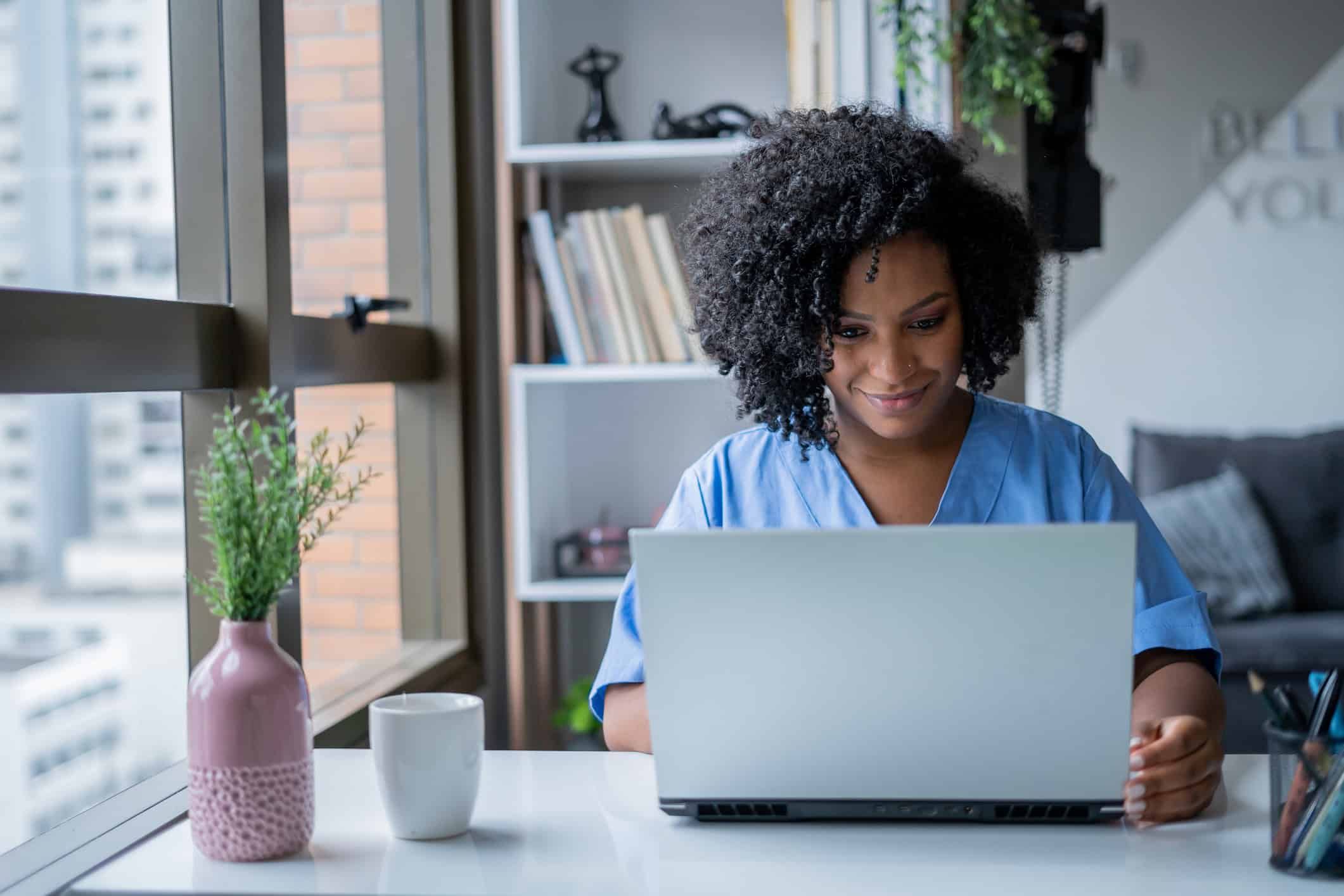 Woman in scrubs sitting in front of a computer