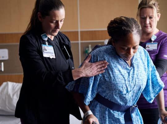 Healthcare professionals assisting patient with mobility and recovery support in clinical setting.