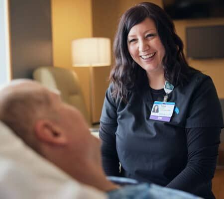 Healthcare professional wearing RN badge smiling while speaking with patient in medical facility.