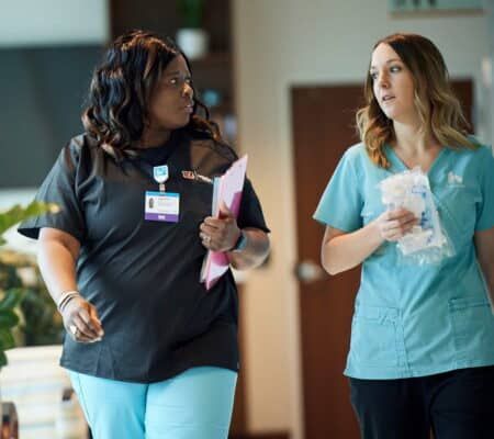 Two healthcare professionals walking and discussing patient care in a clinical hallway setting.