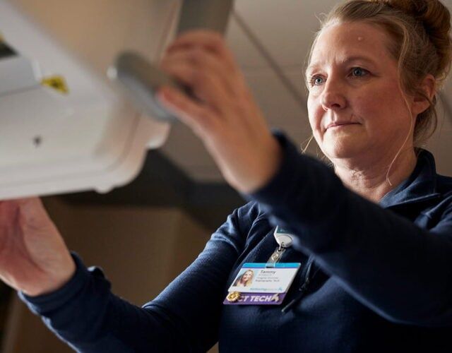 Healthcare professional wearing ID badge examining medical chart on clipboard during patient care.
