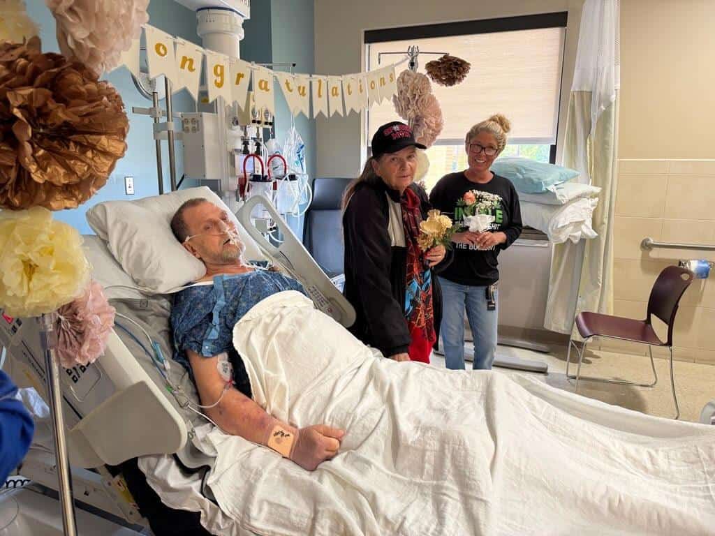 Patient in hospital bed receiving congratulatory visit from family members celebrating recovery milestone.