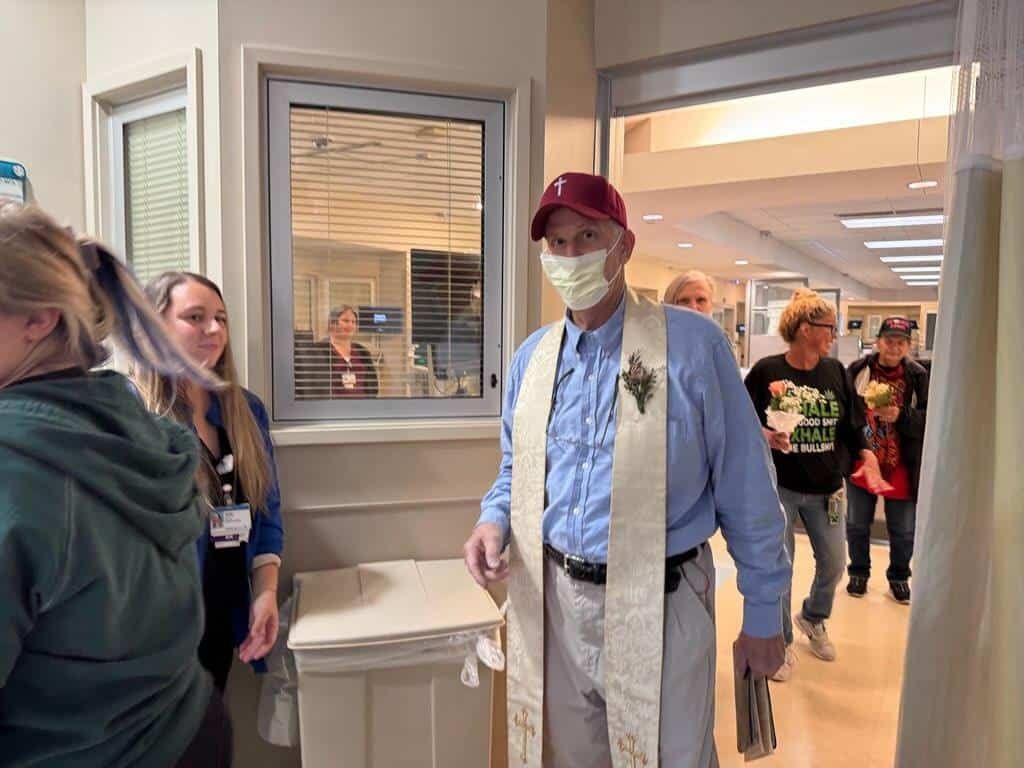 Man in blue shirt and burgundy cap tours Kettering Health facility with visitors and staff present.