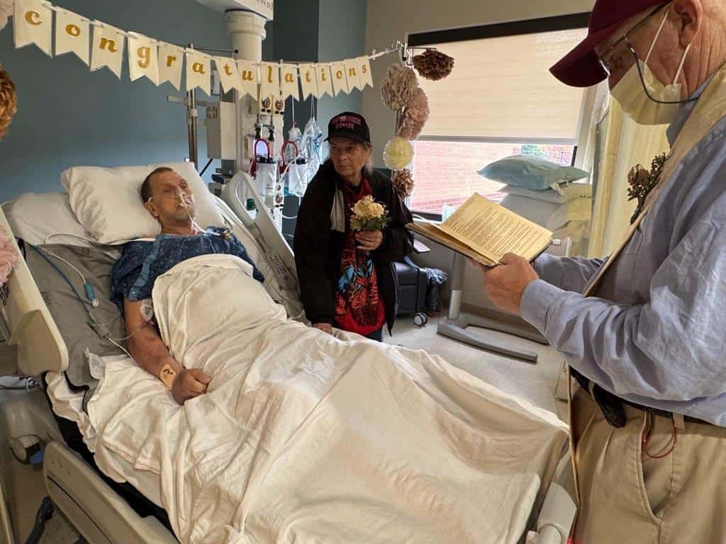 Patient in hospital bed receives visitors during recovery, congrats banner visible in room.