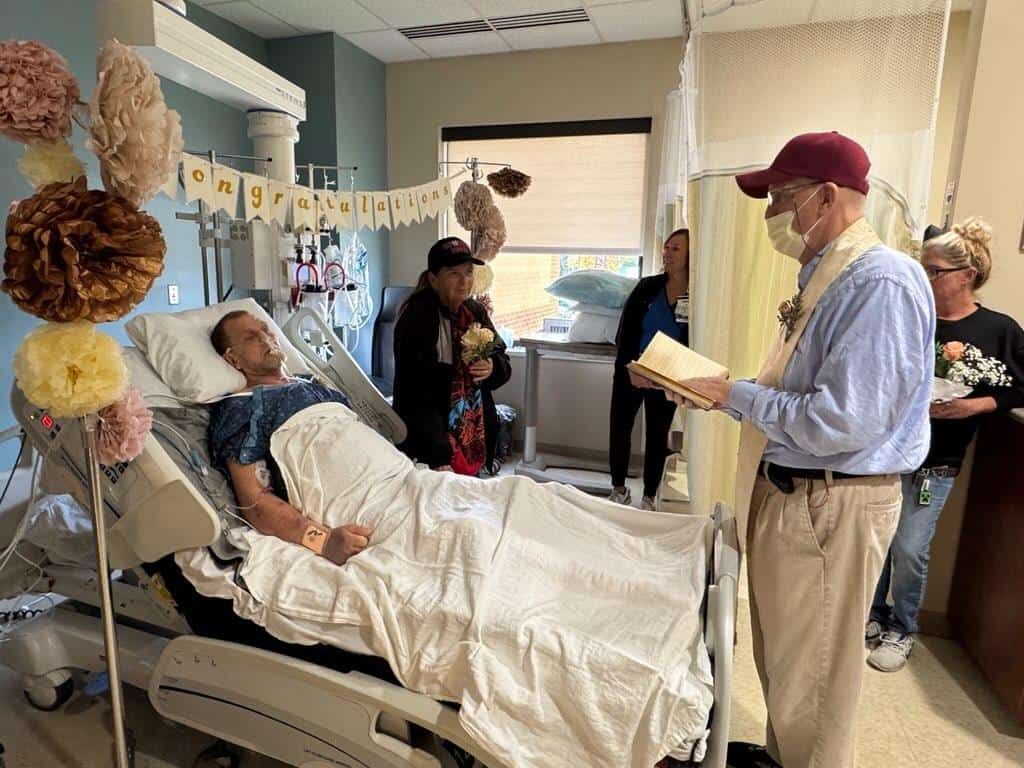 Patient in hospital bed receives visitors during recovery celebration with congratulations banner and decorations.