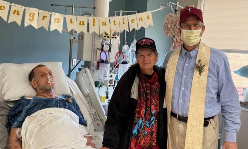 "Patient in hospital bed receives visit from two supporters wearing ""Congratulations"" banner in background."