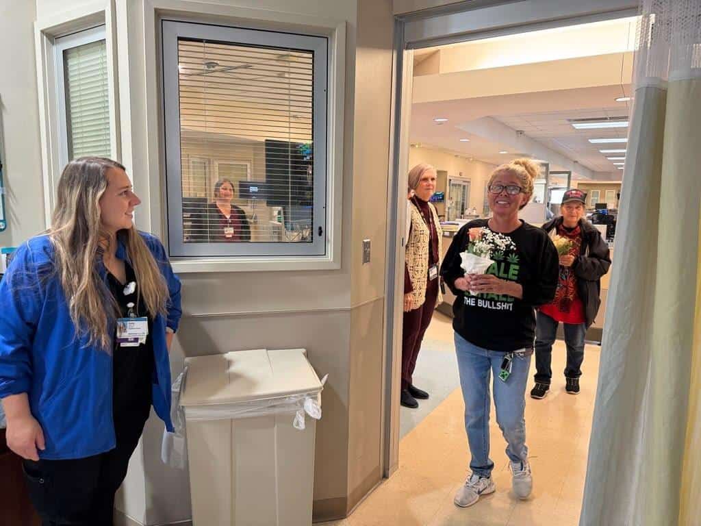 Staff member in blue jacket greeting visitors in modern Kettering Health facility hallway.