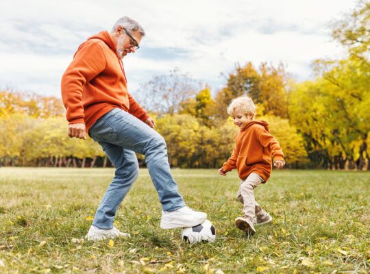 Happy family grandfather and grandson play football on lawn in the park