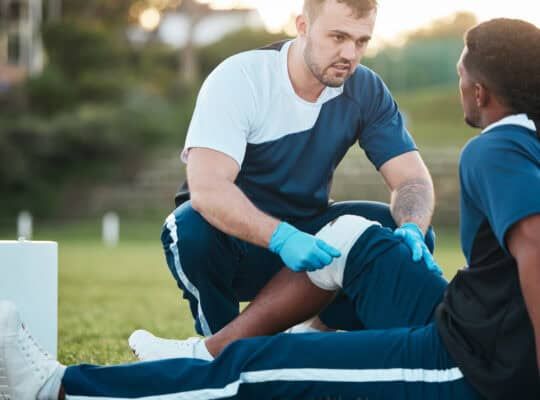 Sports, injury and man with bandage for accident, emergency and first aid for muscle sprain on field. Fitness, healthcare and medic with athlete with knee pain from exercise, workout and training
