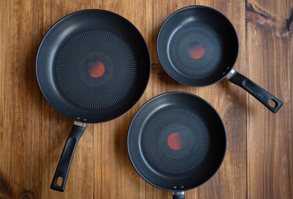Three black non-stick frying pans on a wooden table, showing different sizes of versatile kitchen cookware