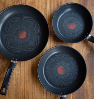 Three black non-stick frying pans on a wooden table, showing different sizes of versatile kitchen cookware