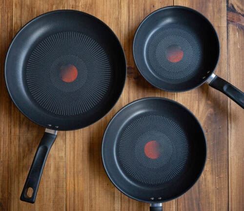 Three black non-stick frying pans on a wooden table, showing different sizes of versatile kitchen cookware