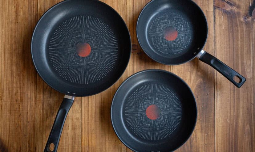Three black non-stick frying pans on a wooden table, showing different sizes of versatile kitchen cookware
