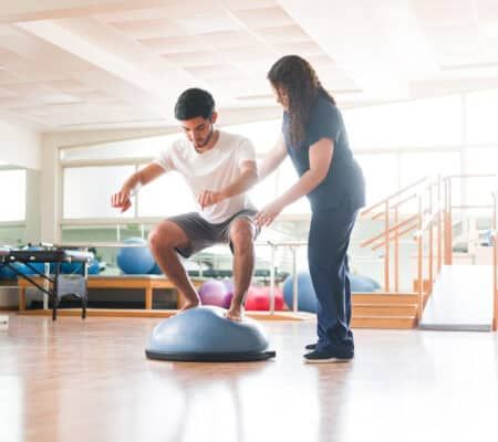 A male athletic patient standing on a balance fitness ball during physical therapy.