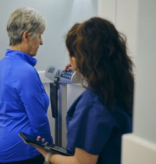A nurse in a doctor’s office, wearing a senior female patient on a scale.