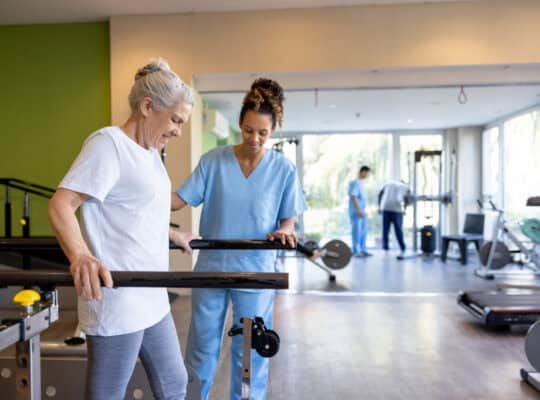 Senior woman in physical therapy walking on the bars with the help of her therapist - orthopedic medicine concepts